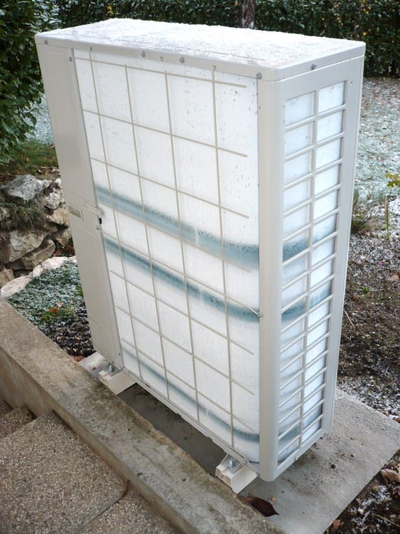 Unité extérieure d'une pompe à chaleur complètement recouverte d'un bloc de givre en hiver.